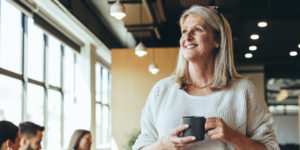 Very nice lady smiling drinking coffee walking in her office looking off to the side
