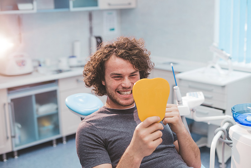 Very nice guy smiling in dental chair looking into mirror