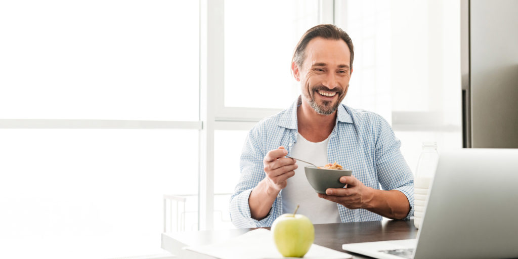 Nice guy eating breakfast at home in front of a laptop